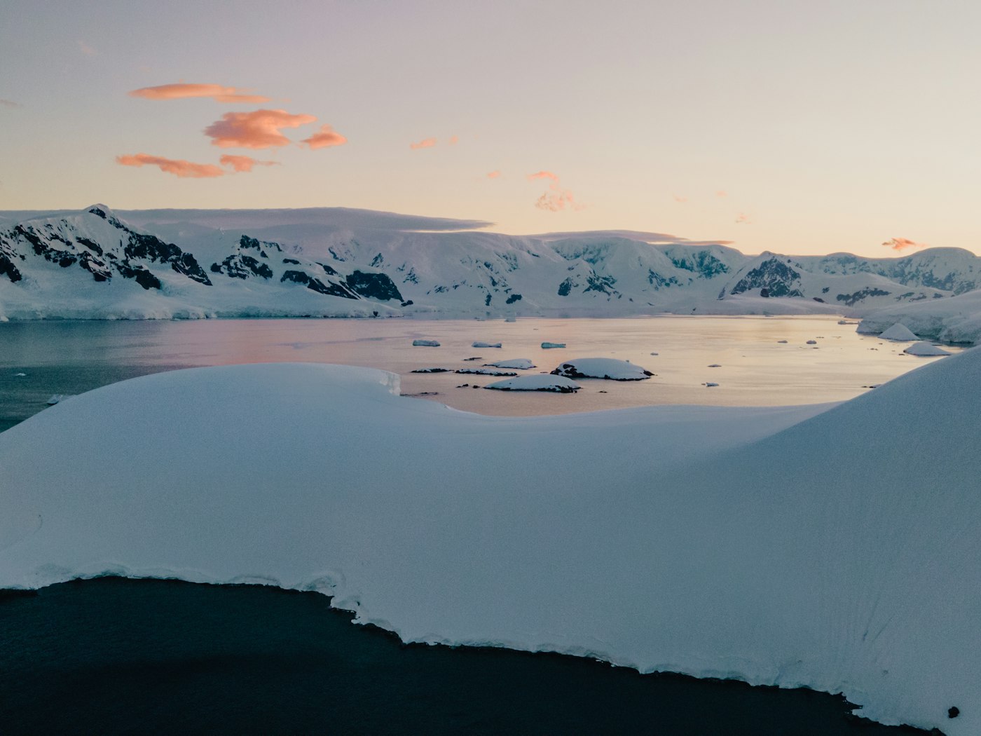 Pink evening light over snowy mountains and still water on the Antarctic Peninsula